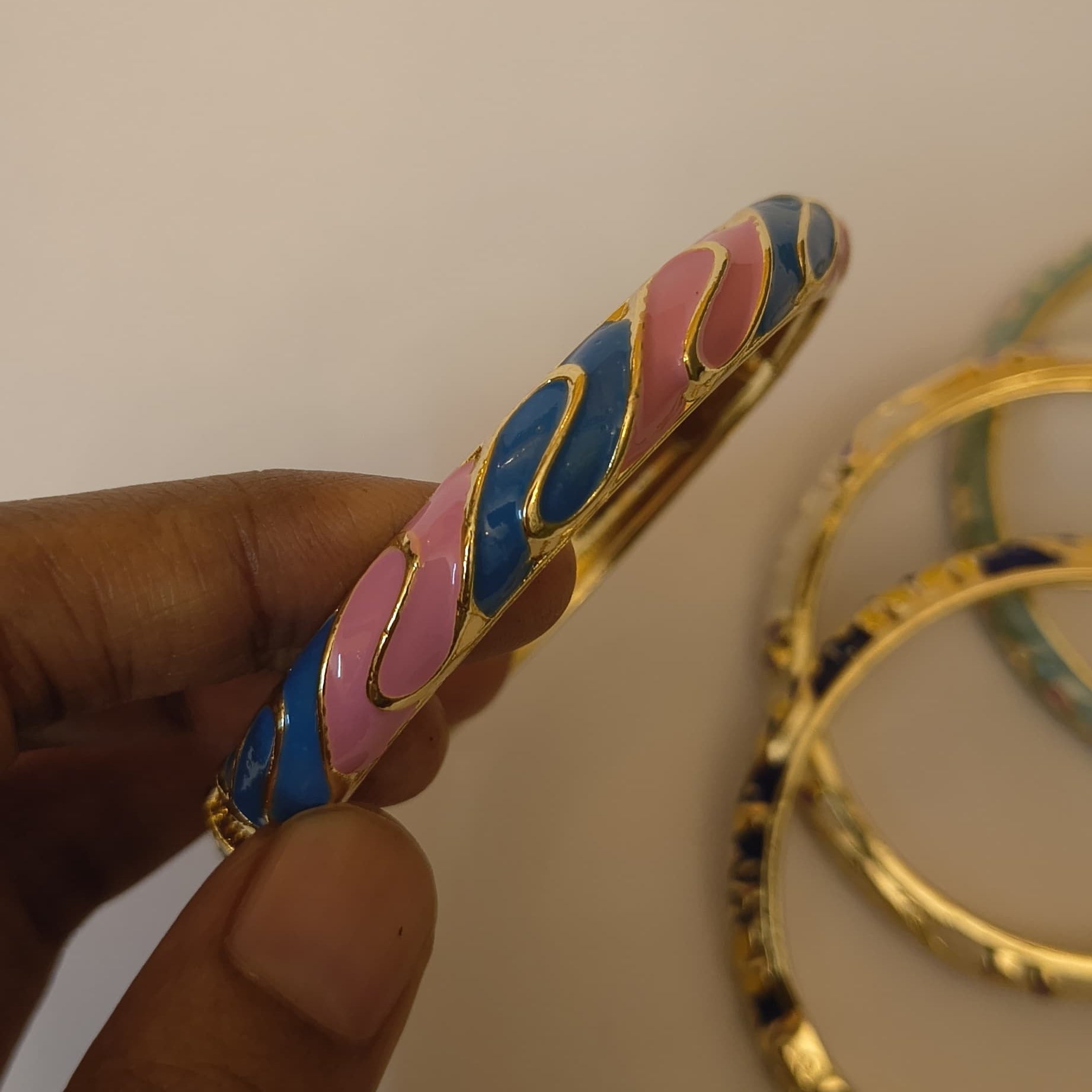 Pink and blue enamel wave bangle with gold-tone trim, held in hand